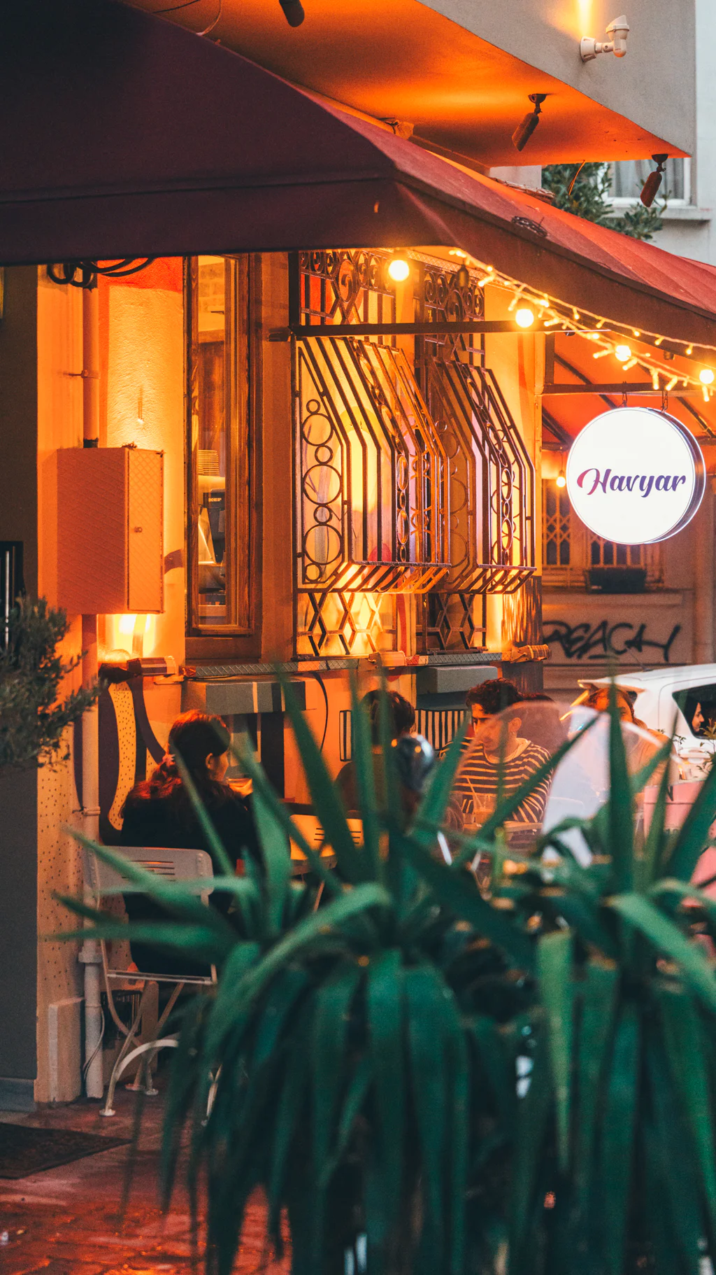People dining outdoors at a warmly lit cafe with a sign reading 'Havyar'.