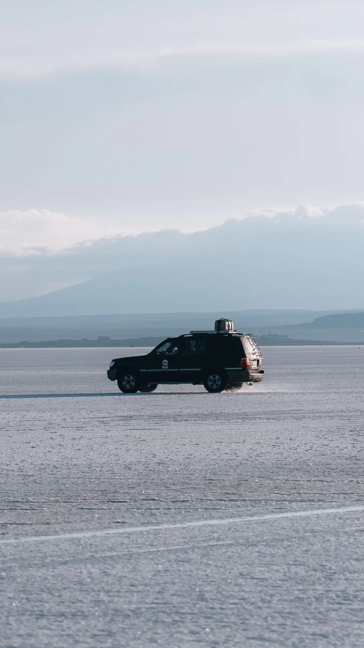 Black SUV driving on a vast flat landscape with mountains in the background.