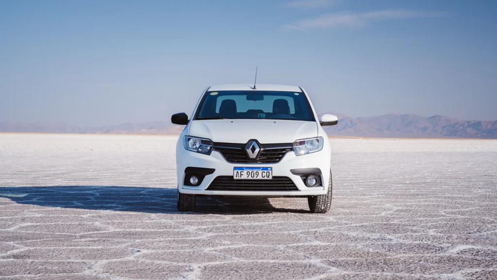 Front view of a white Renault car on a salt flat with mountains in the background.