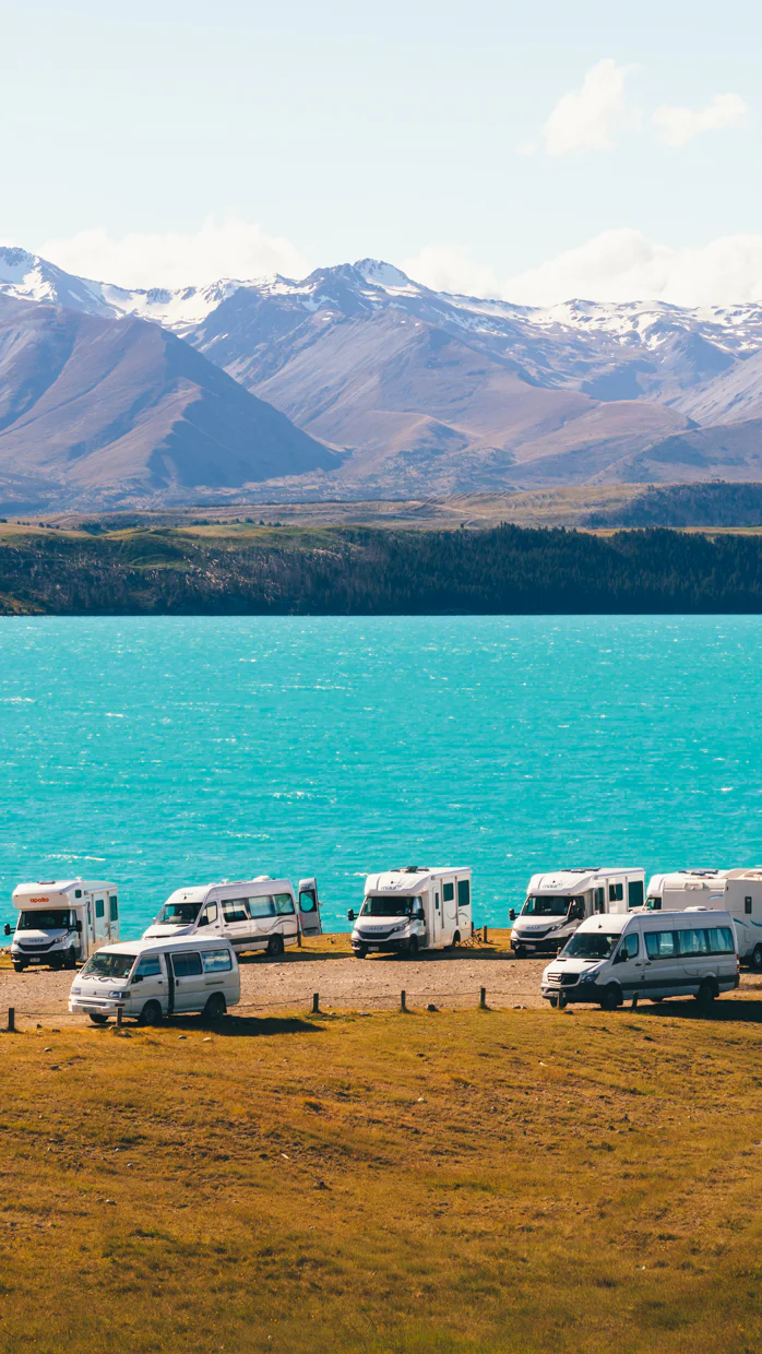 Camping vans parked by a turquoise lake with mountains in the background.