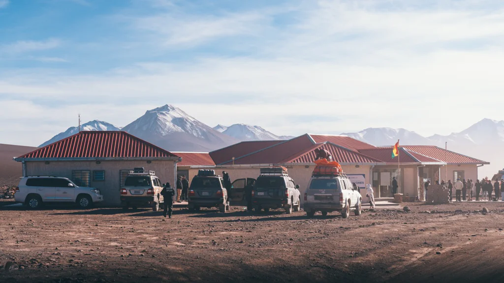 Rural buildings with parked vehicles and mountains in the background under a clear sky.