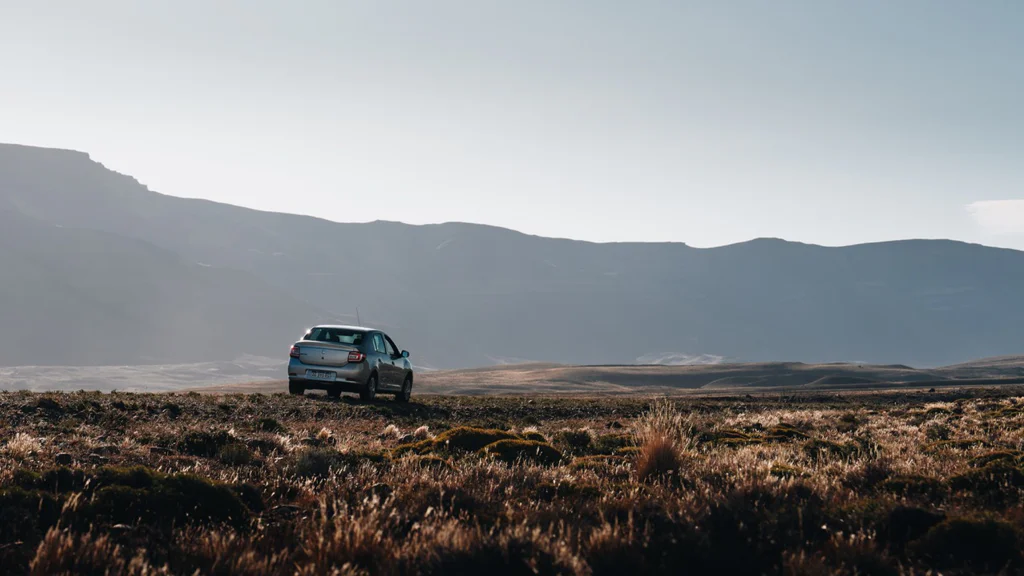 A car driving on a road with mountains in the background under a clear sky.
