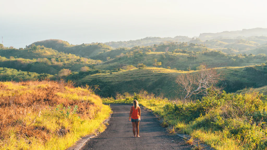 Person walking alone on a road through a green and hilly landscape.