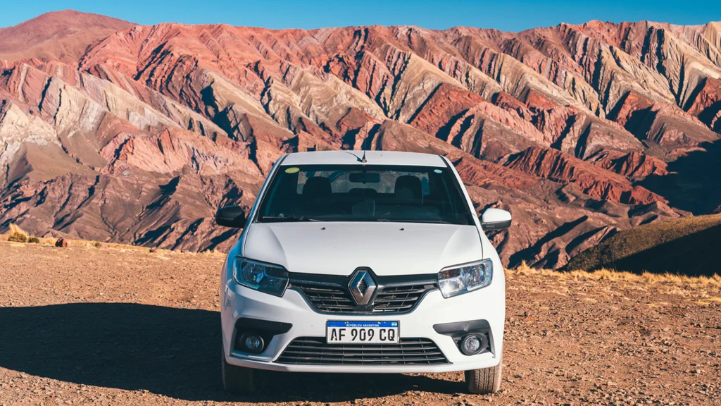 White Renault car parked on a dirt road with layered mountains in the background.