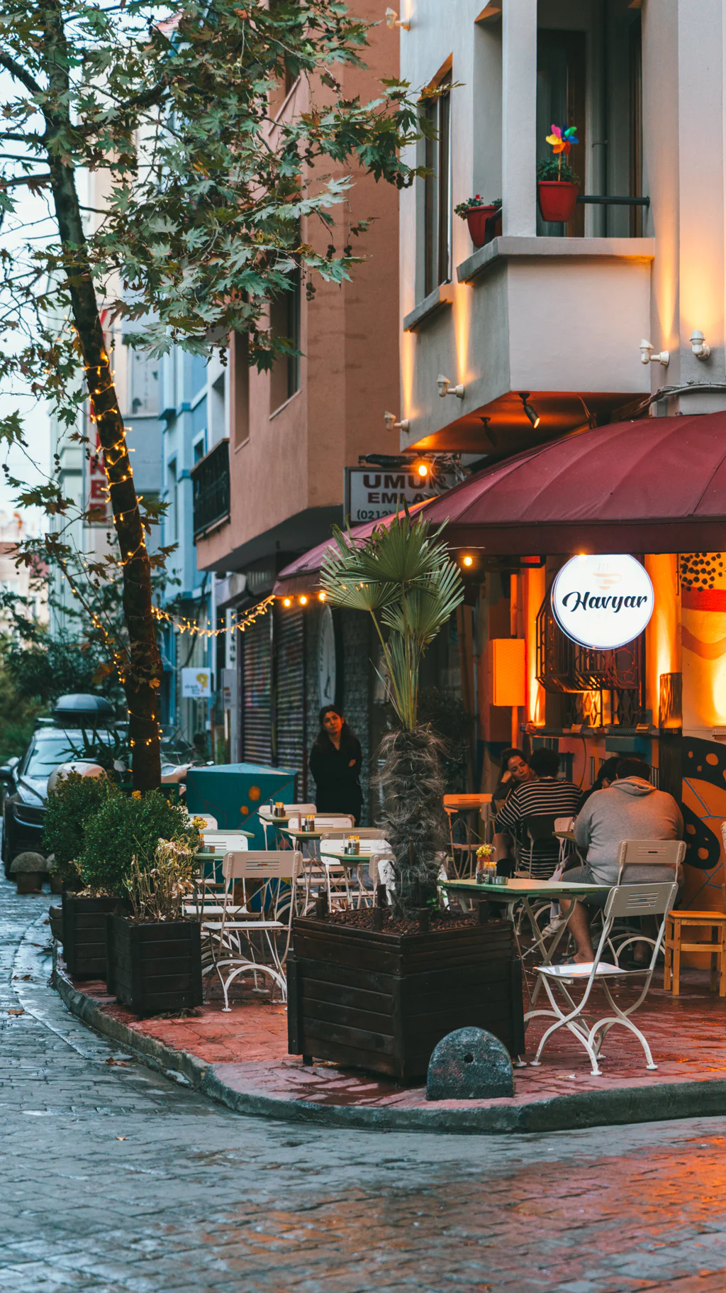 Outdoor café with people sitting at tables on a cobblestone street in the evening.