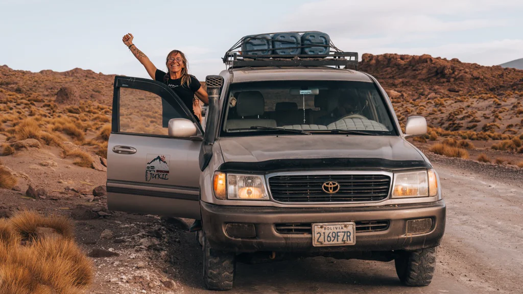 Woman standing beside an off-road vehicle in a desert landscape with gear on the roof.