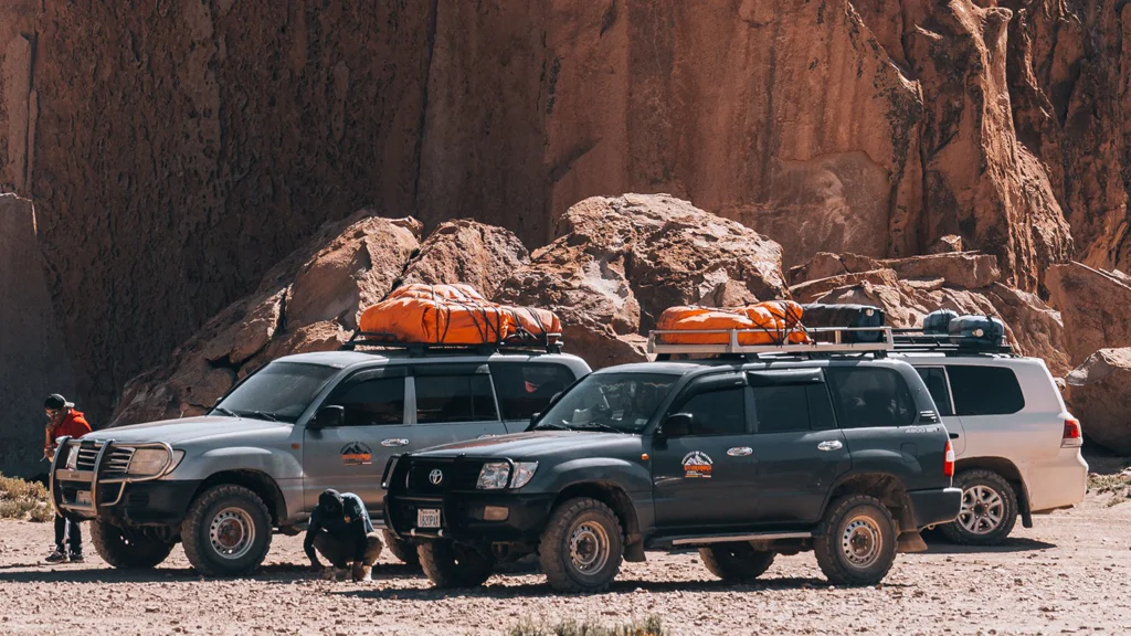 Three off-road SUVs parked on rocky desert terrain with camping gear on their roofs.