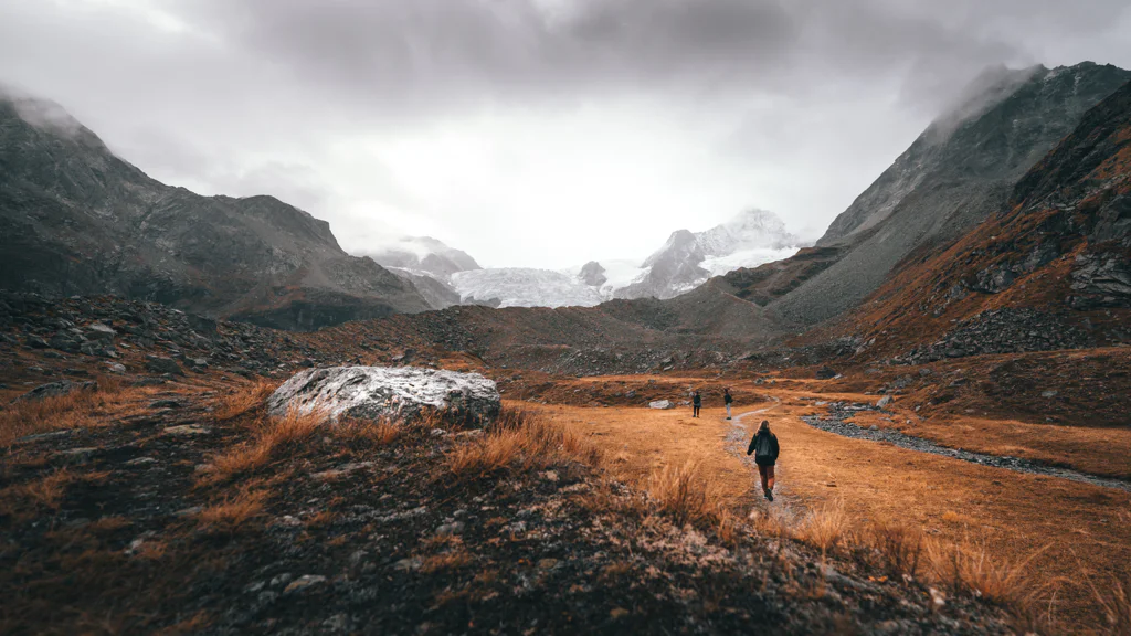 Hikers walking through a mountain valley with autumn grass and cloudy sky.