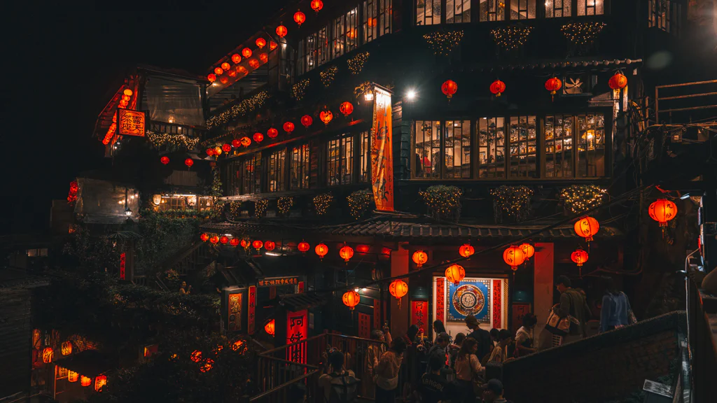 Nighttime street scene in Jioufen with glowing red lanterns and people walking near traditional buildings.