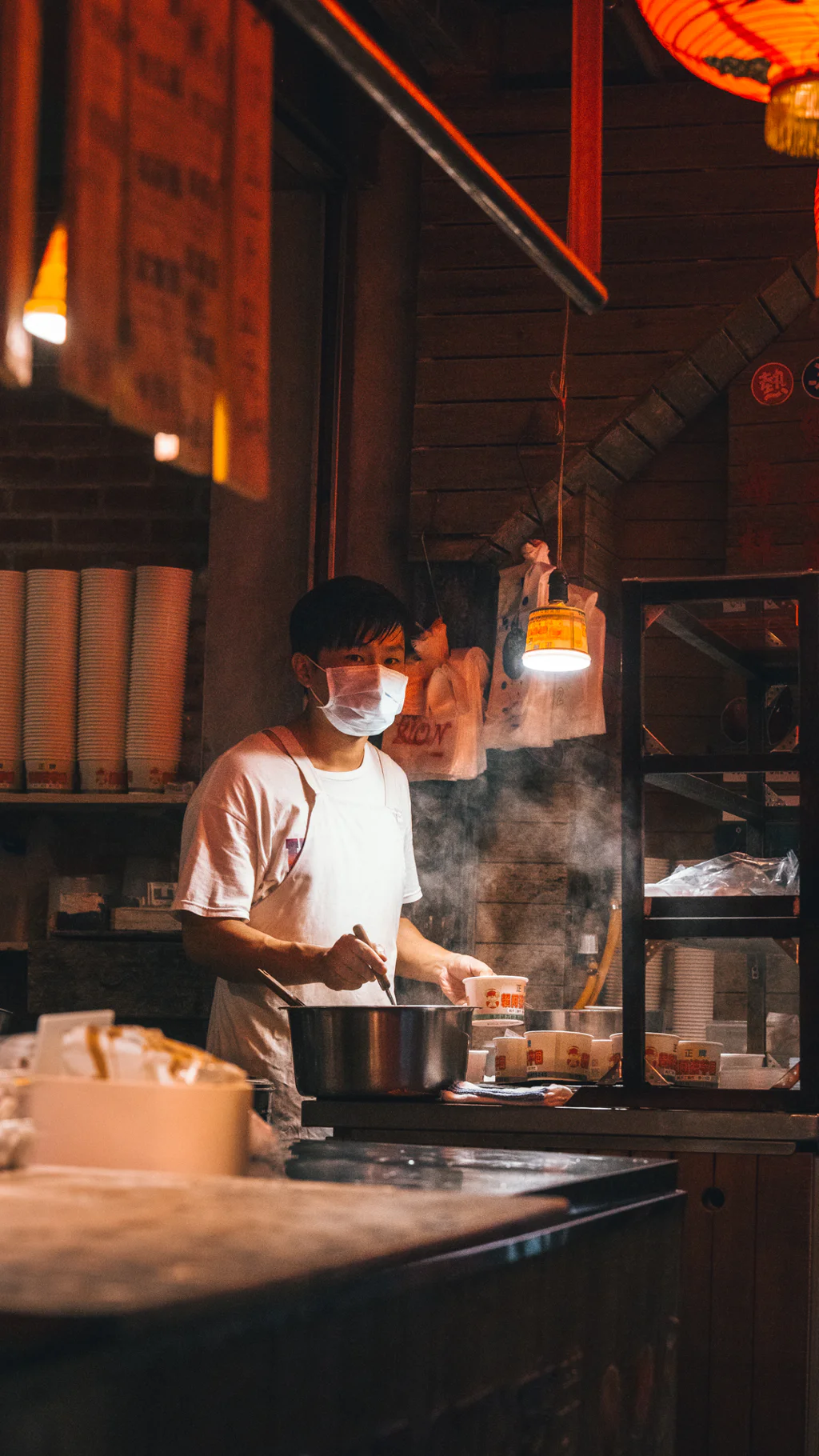 A masked street food vendor cooking at a food stall in Jioufen with steam rising from a pot.
