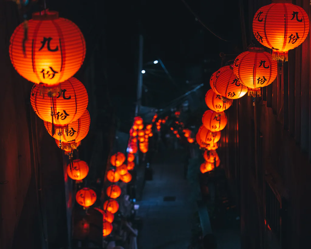 Rows of red lanterns glowing warmly along a narrow street at night in Jioufen.