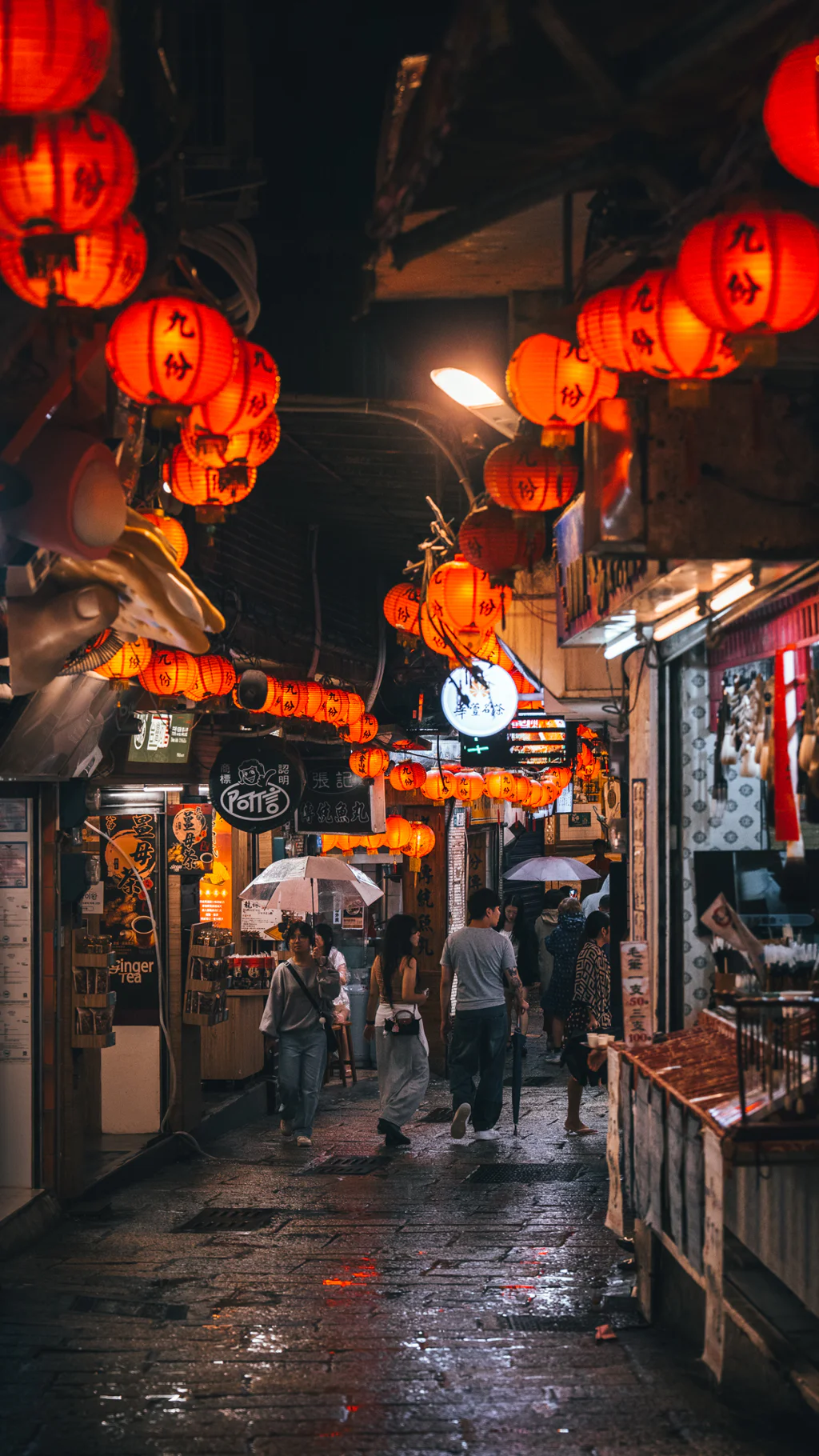 Nighttime street market in Jioufen with red lanterns and people walking under umbrellas.